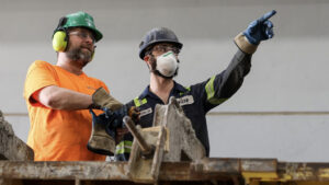 Two men wearing safety gear stand together, holding a piece of wood, highlighting MCON careers in the construction industry.