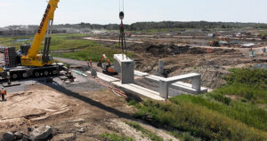 A crane lifts a concrete bench high into the air at a construction site.