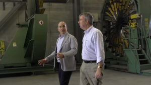 Jim Watson and another man stand in front of a large industrial machine, discussing its features and operation.